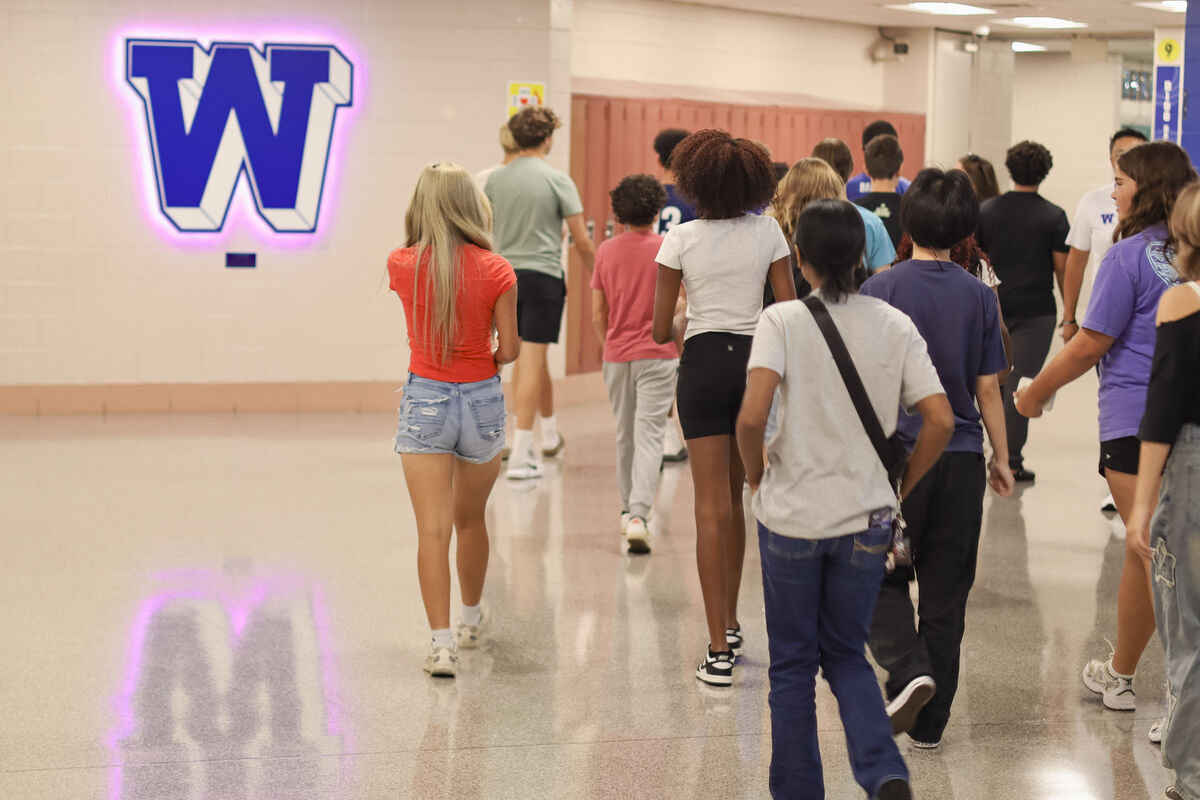 A group of students walks down a hallway with a large illuminated 'W' logo on the wall.
