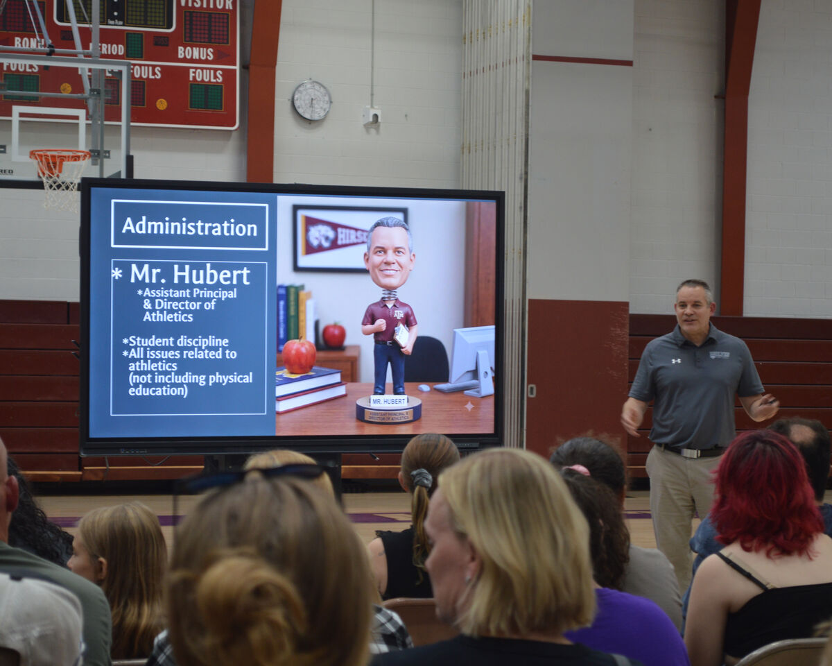 A man presents information on a large screen displaying 'Administration' and details about Mr. Hubert.