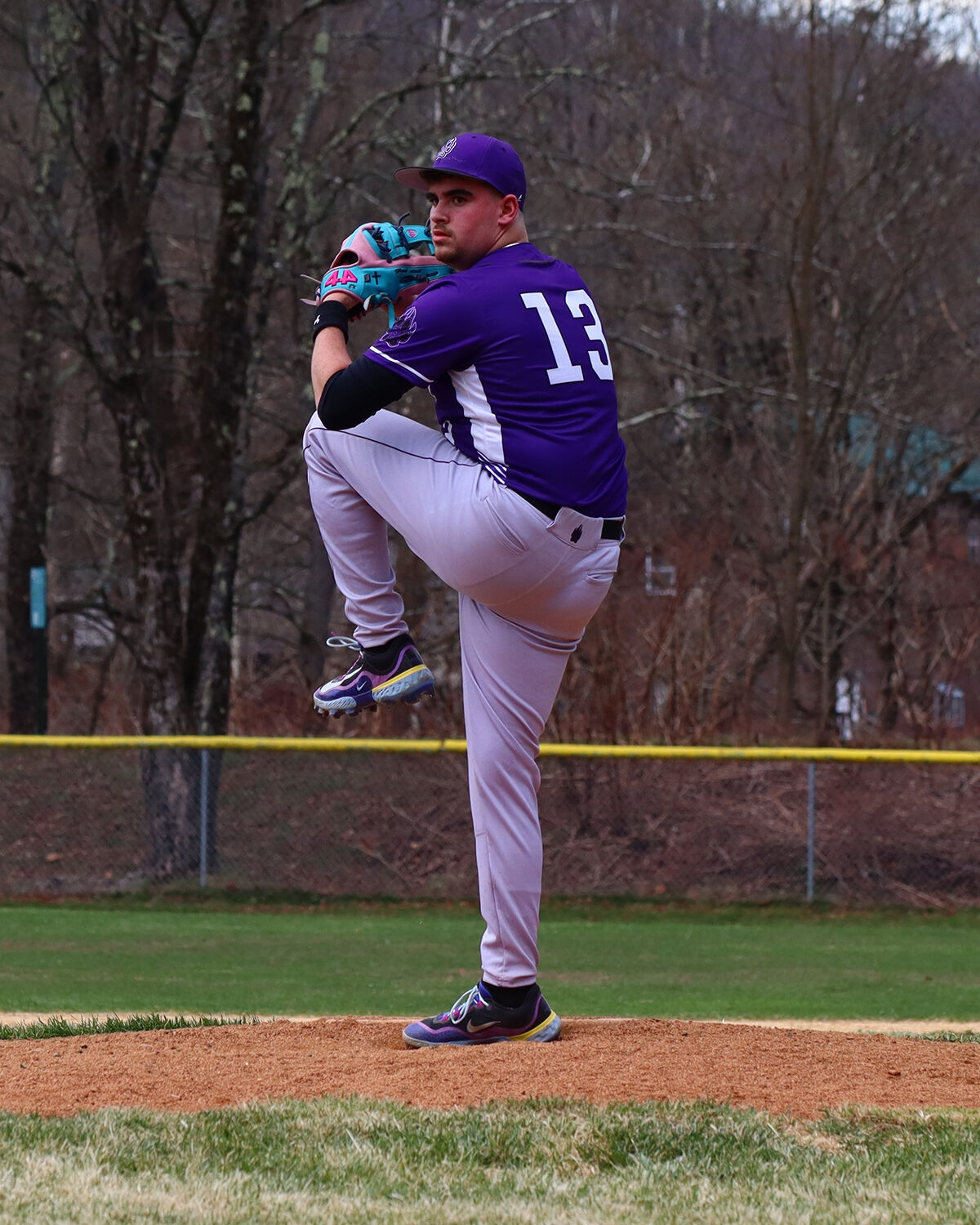 A baseball pitcher in a purple uniform with the number 13 on his back prepares to throw.
