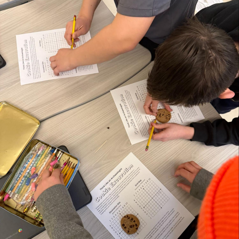 Students are engaged in a 'Cookie Excavation' activity, using pencils and worksheets.