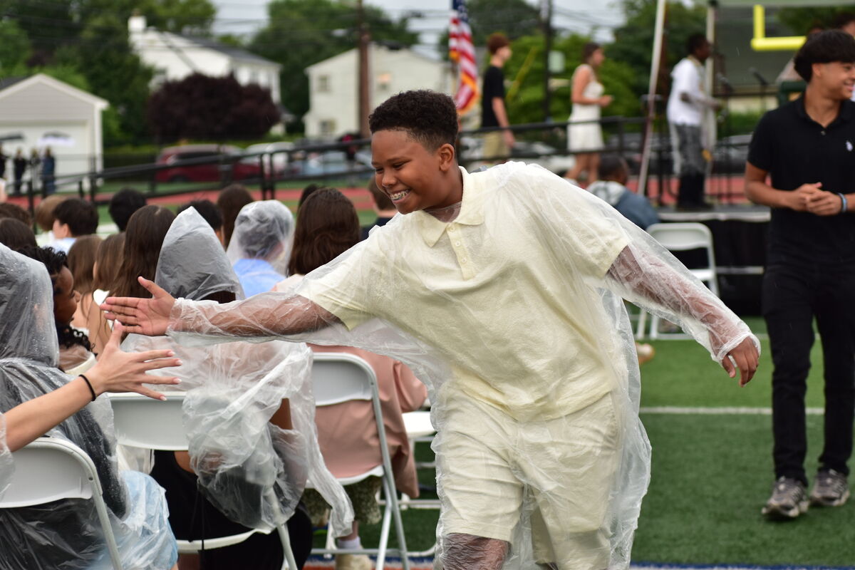 A young person in a clear poncho smiles and reaches out to someone in the foreground.