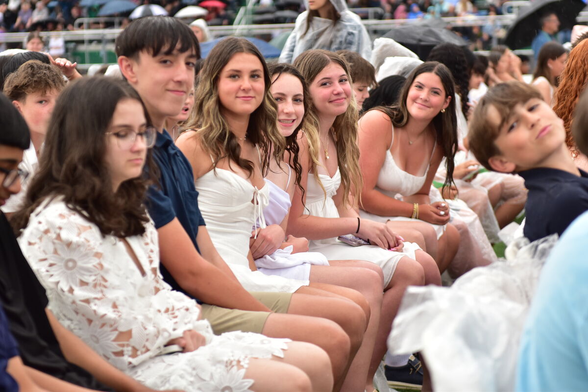 A group of young people in white attire sit together, some smiling at the camera.