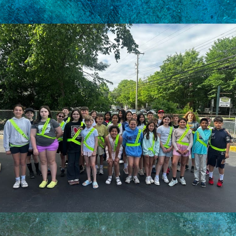 A diverse group of children wearing bright yellow safety vests stand together outdoors.