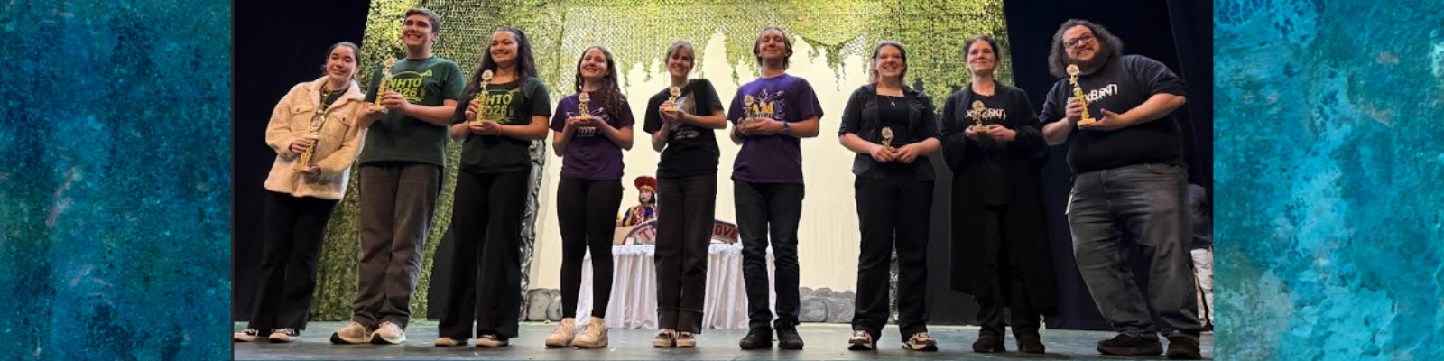 A group of smiling individuals stand on a stage, each holding a trophy.