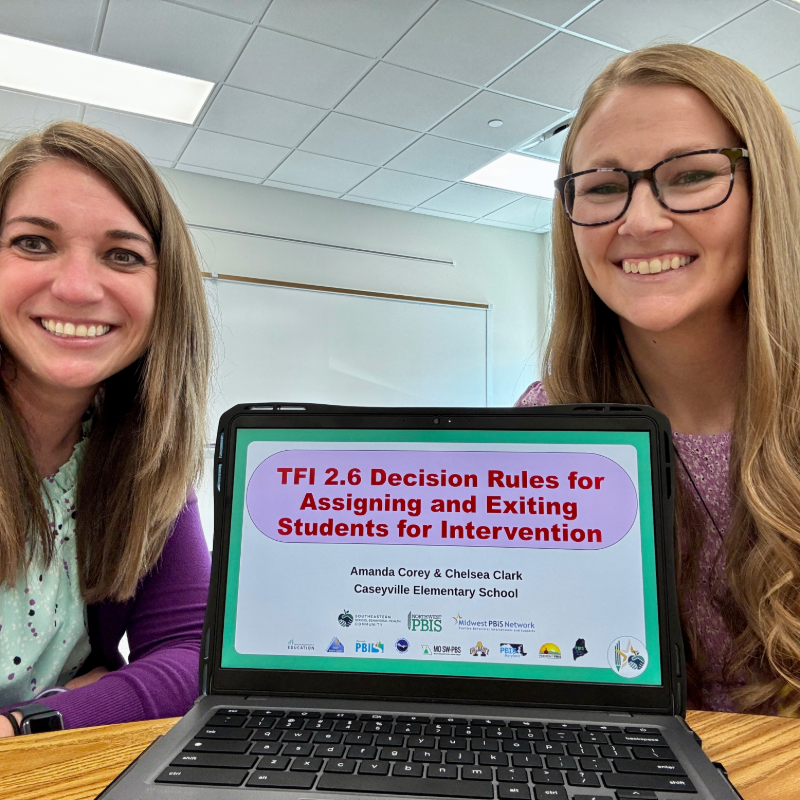 Two smiling women present a laptop screen with the title 'TFI 2.6 Decision Rules for Assigning and Exiting Students for Intervention'.