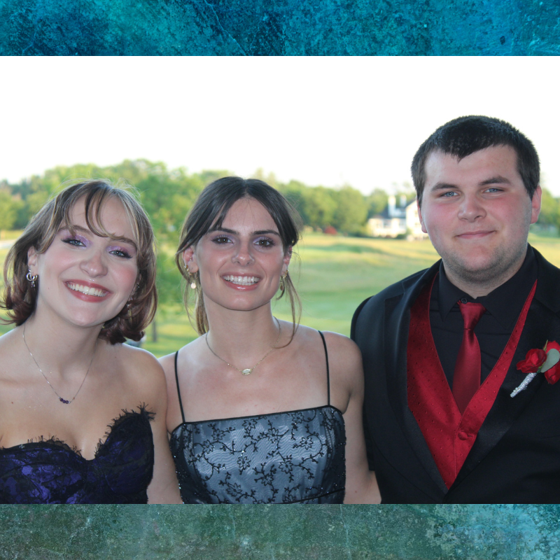 Three young people in formal attire smile for a photo outdoors.