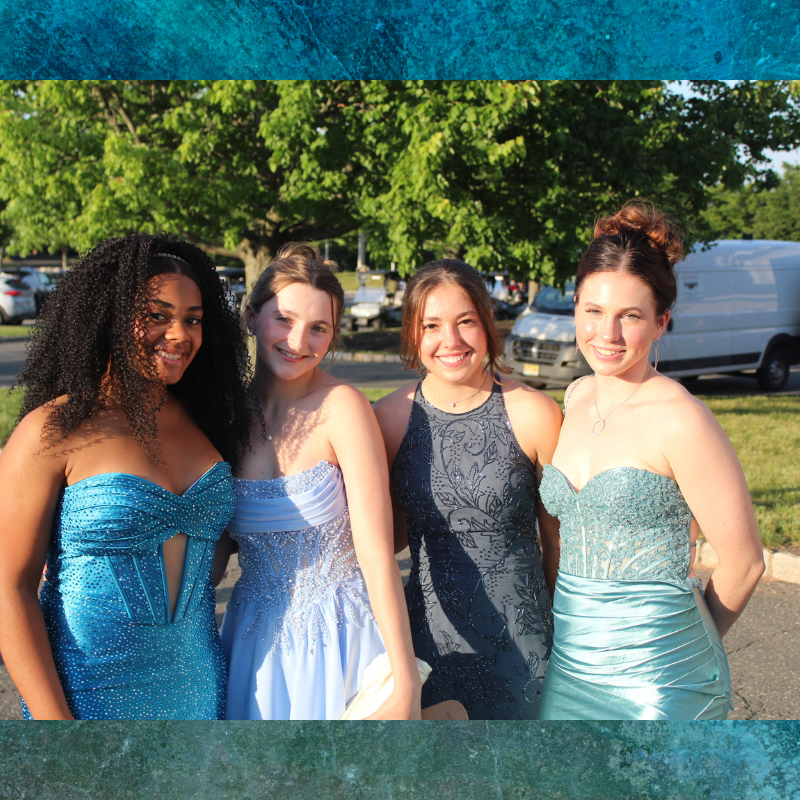 Four young women in elegant gowns smile for a photo outdoors.