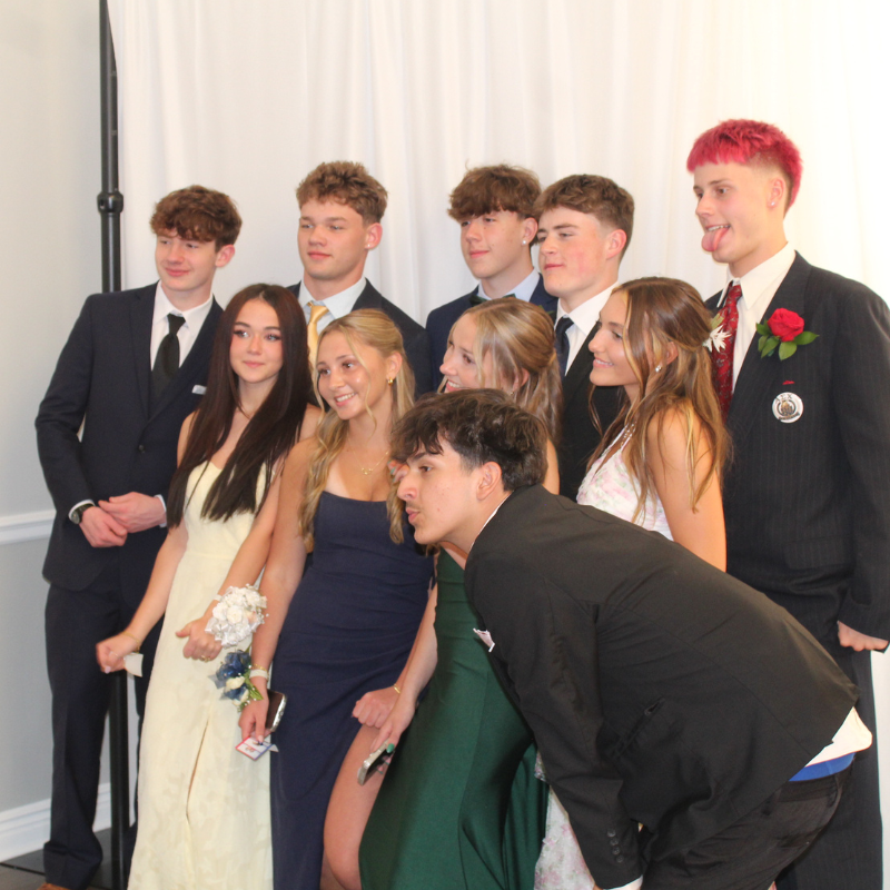 A group of young people in formal attire pose for a photo against a white backdrop.