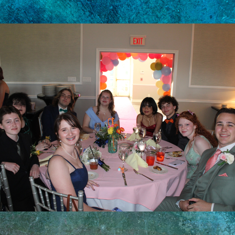 A group of young people in formal attire sit around a pink-clothed table at an event.