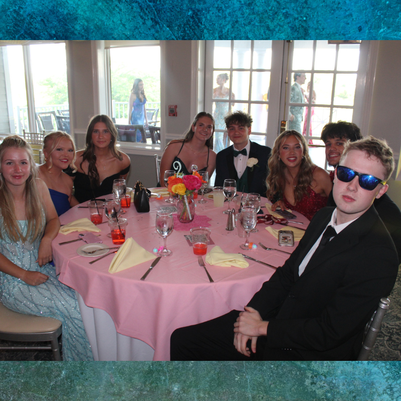 A group of young people in formal attire sit around a round table at an event.