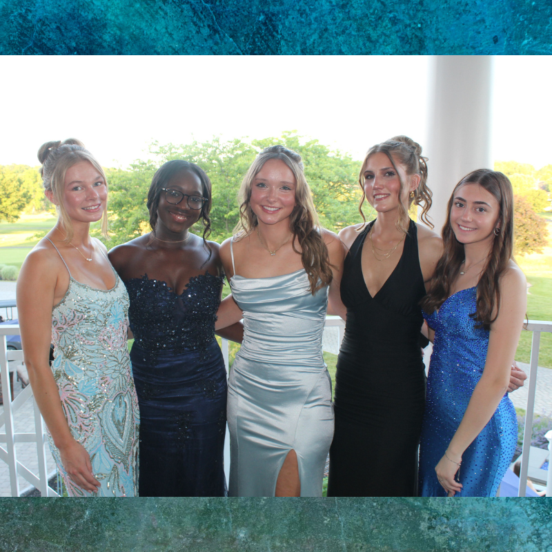 Five young women in elegant formal dresses pose for a photo outdoors.
