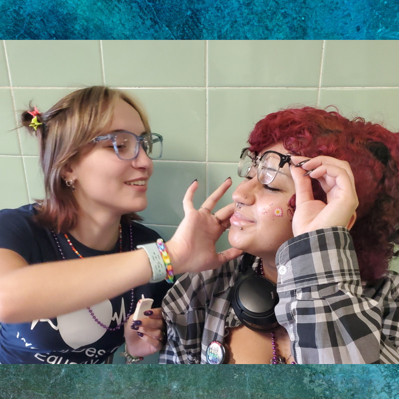 Two friends are applying glitter makeup to each other's faces.