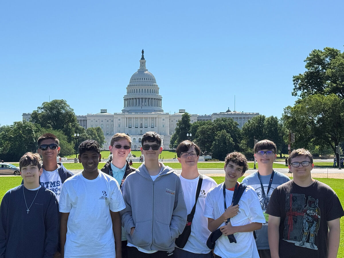 A group of young people stand smiling in front of the U.S. Capitol building on a sunny day.