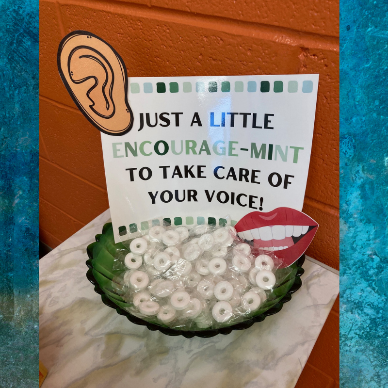 A sign reads 'JUST A LITTLE ENCOURAGE-MINT TO TAKE CARE OF YOUR VOICE!' above a bowl of mints.