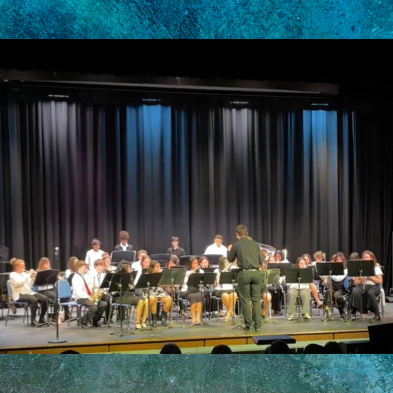 A conductor leads a student orchestra performing on a stage with black curtains.