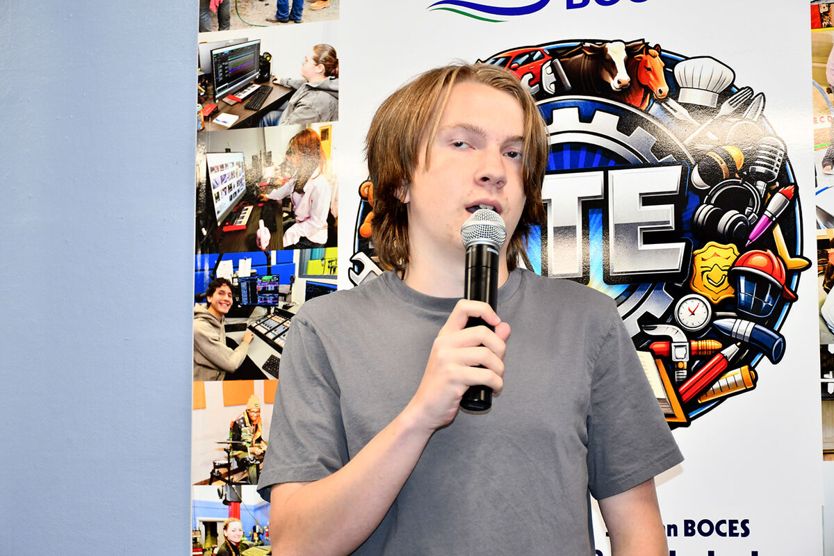 A young person holds a microphone in front of a colorful graphic with various icons.
