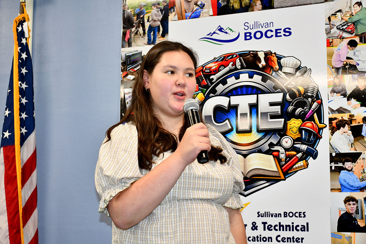 A young woman speaks into a microphone in front of a banner for Sullivan BOCES & Technical Education Center.