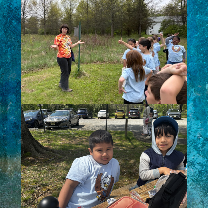 A group of children in light blue shirts listen to a woman in a tie-dye shirt in a grassy outdoor area.