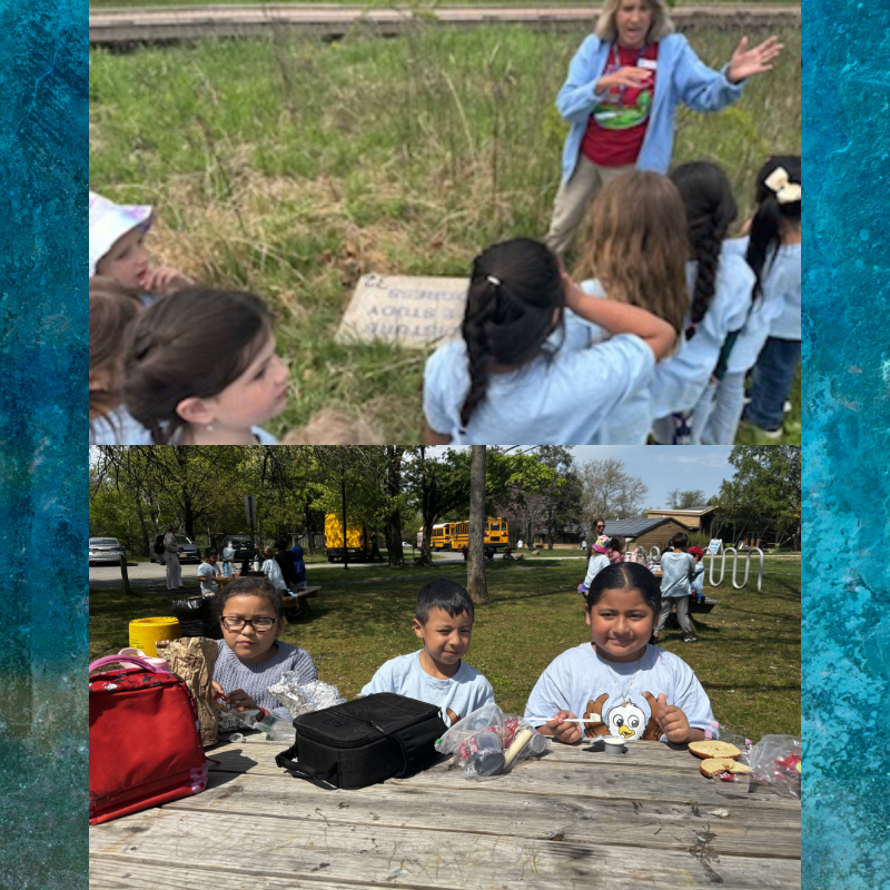 A group of children listen to a woman in a blue jacket in a grassy outdoor setting.