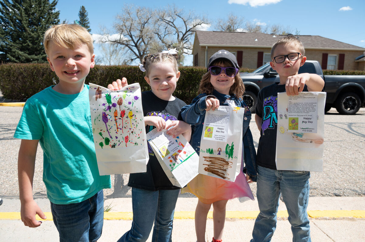 Four children proudly display decorated bags with drawings and text, including "Happy May Day" and quotes from Dr. Seuss.