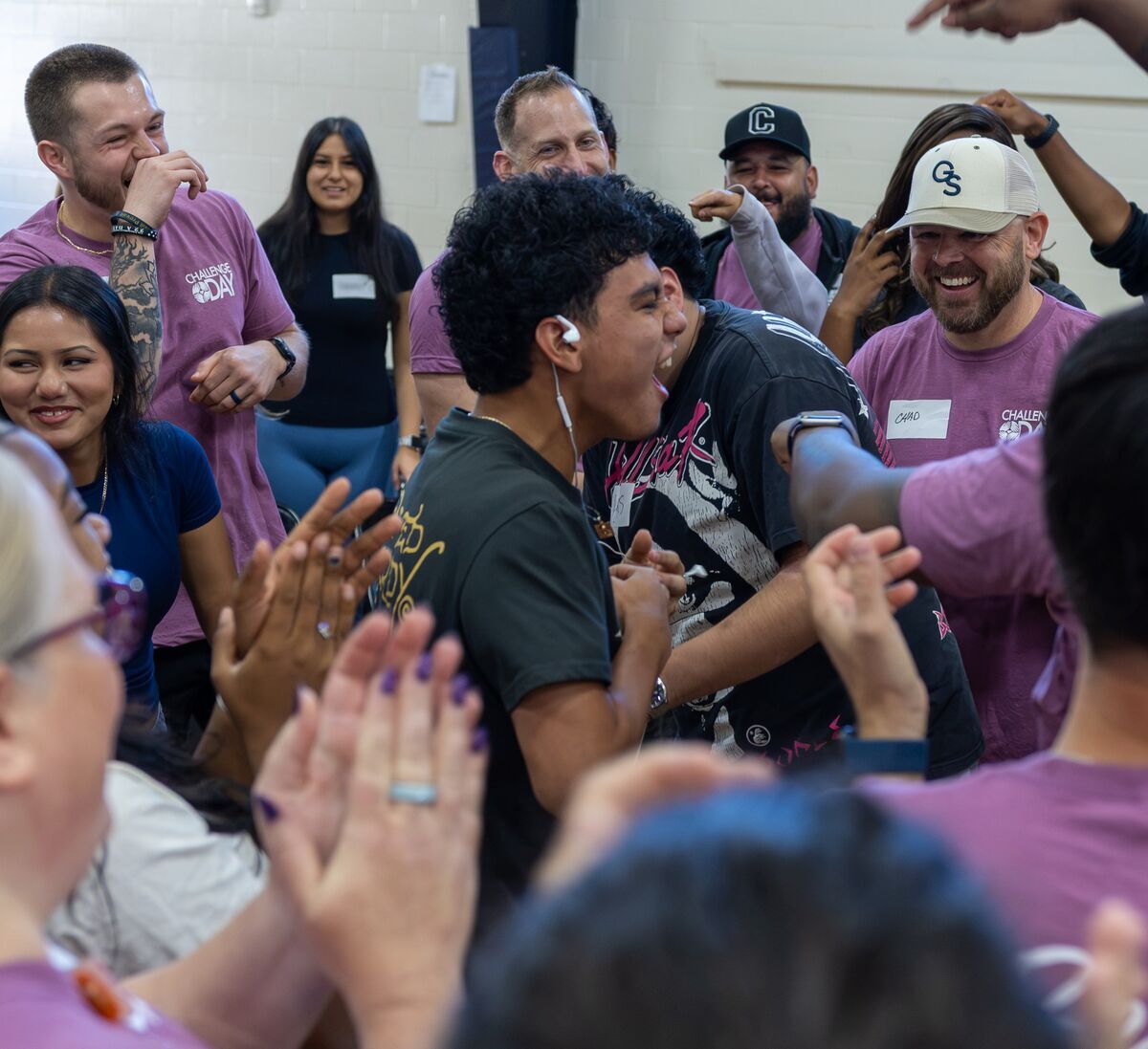 A diverse group of people in purple shirts smile and cheer together indoors.