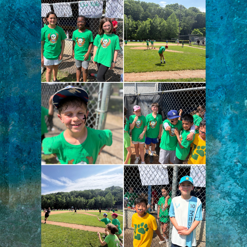 A group of children in green shirts stand near a fence at a baseball field.