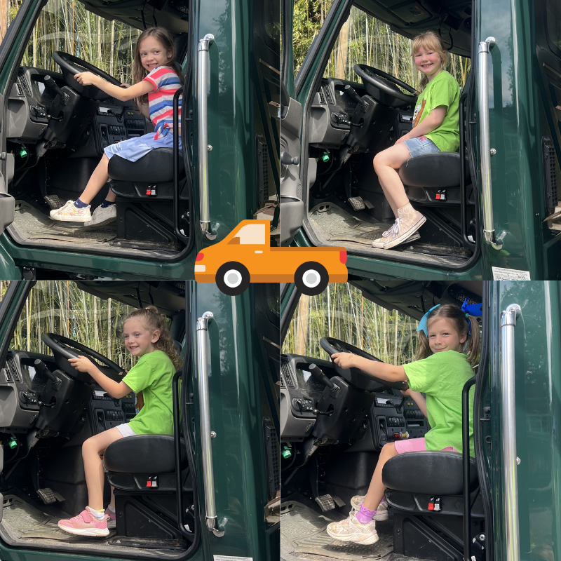 Four young girls sit in the driver's seat of a large green truck, pretending to drive.