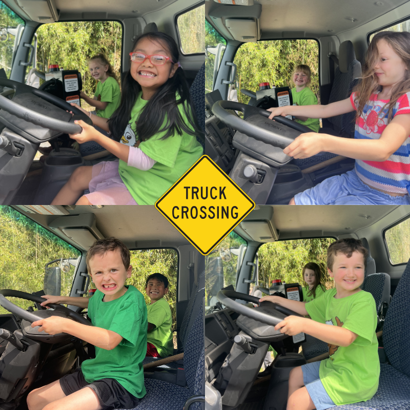 Children in green shirts sit in the driver's seats of a truck, pretending to drive.