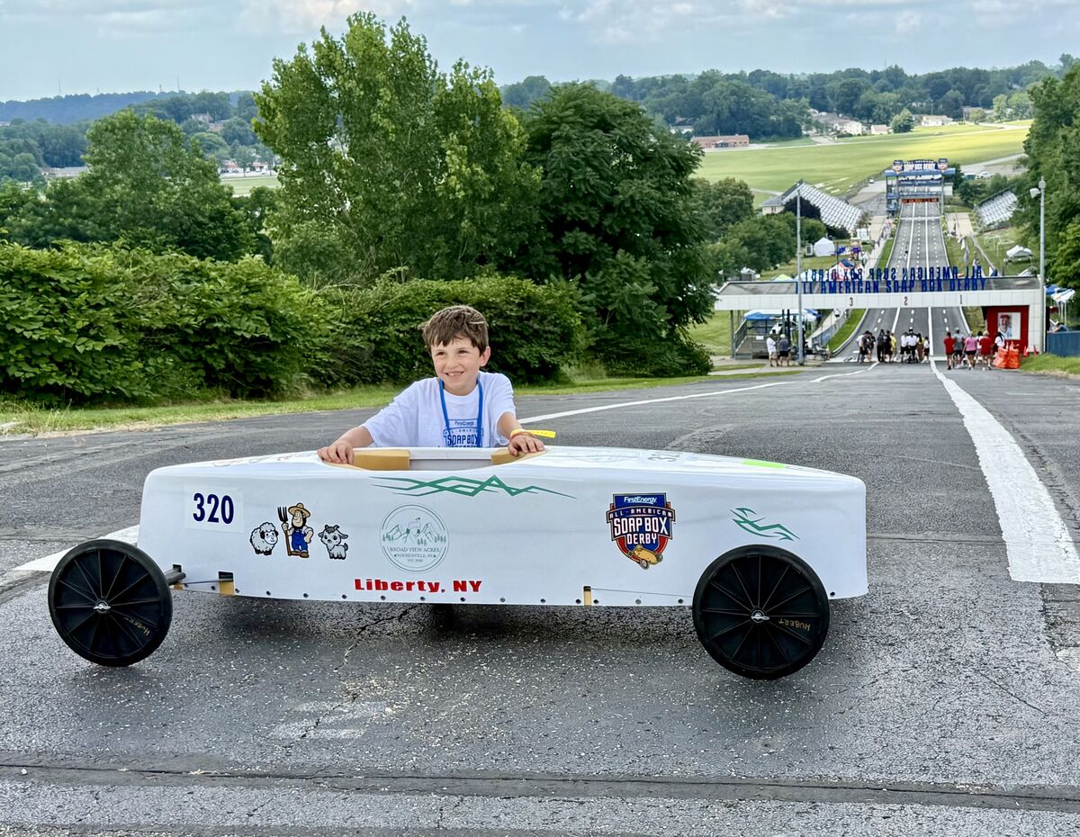 A young boy smiles from inside a white soap box car with the number 320 and "Liberty, NY" on its side.