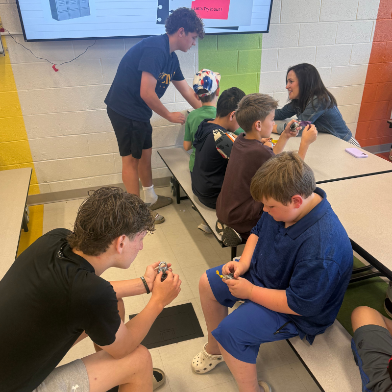 A group of students and an adult are gathered around tables, working with small objects.