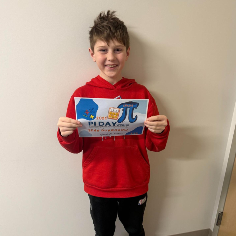A smiling boy in a red hoodie holds a Pi Day award certificate.