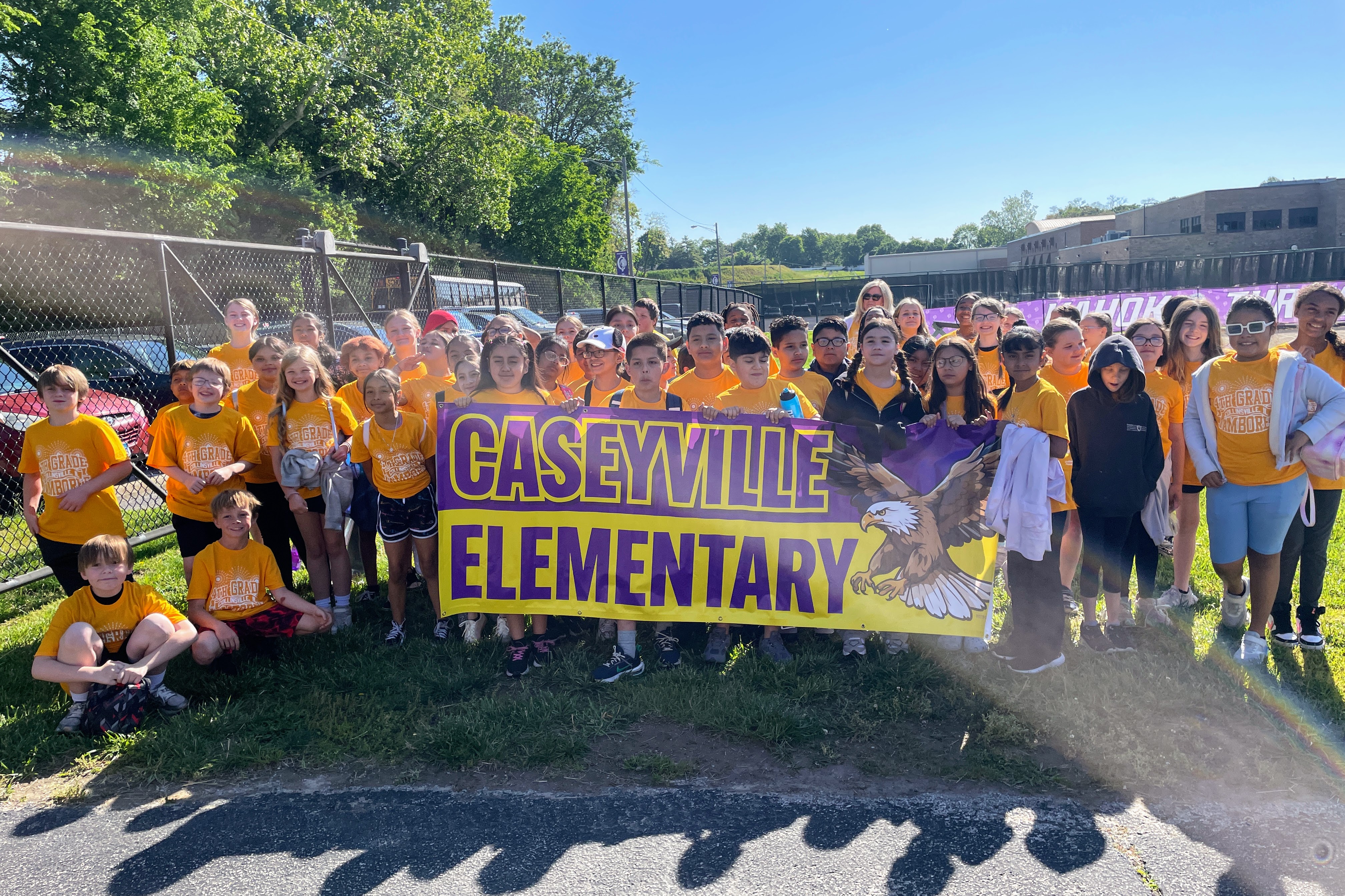 A group of students in orange shirts stand behind a banner that reads 'CASEYVILLE ELEMENTARY' with an eagle graphic.