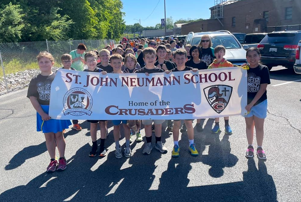 Students from St. John Neumann School hold a banner that reads 'ST. JOHN NEUMANN SCHOOL Home of the CRUSADERS'.