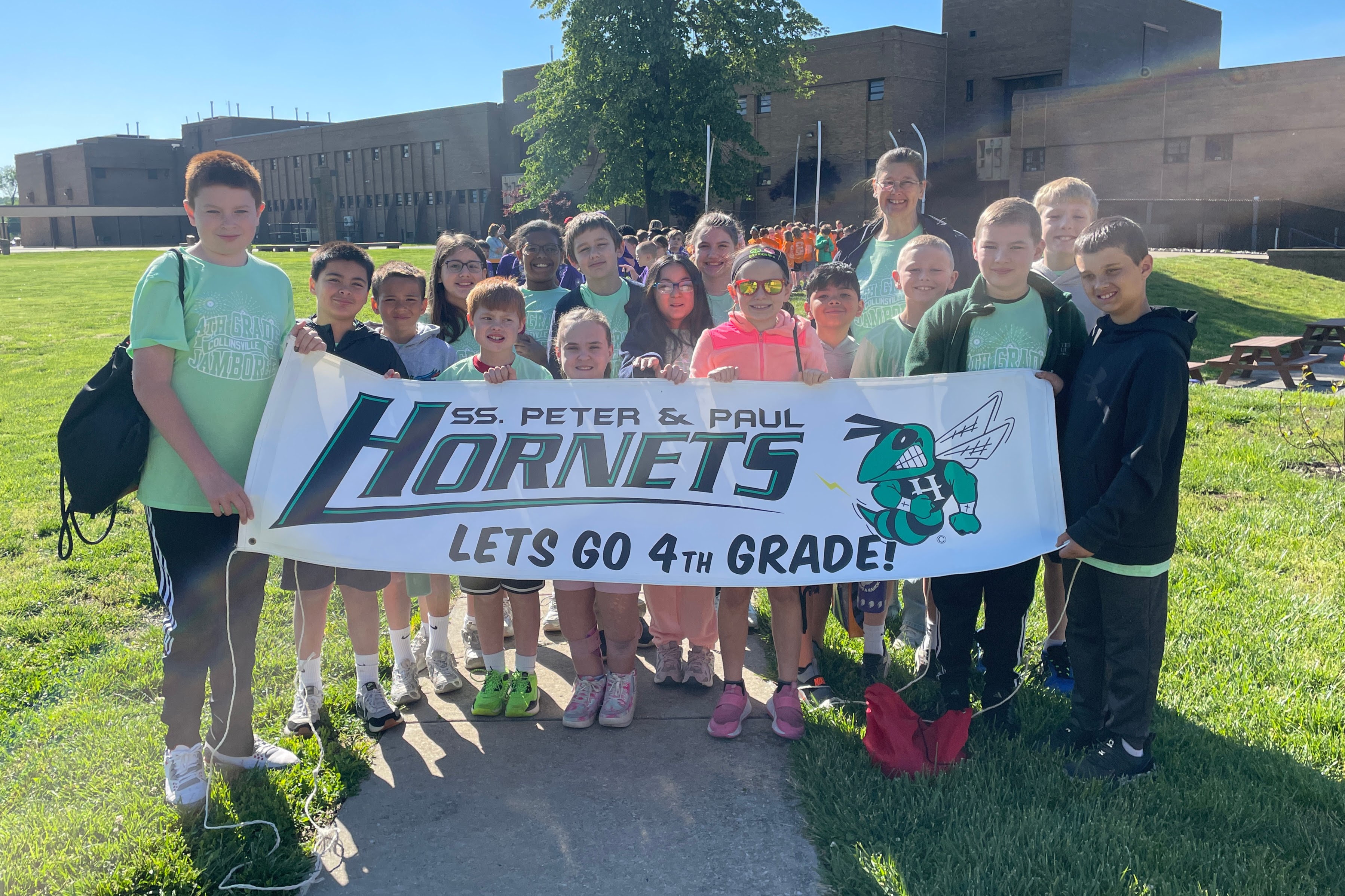 A group of smiling 4th-grade students hold a banner that reads 'SS. PETER & PAUL HORNETS LETS GO 4TH GRADE!'