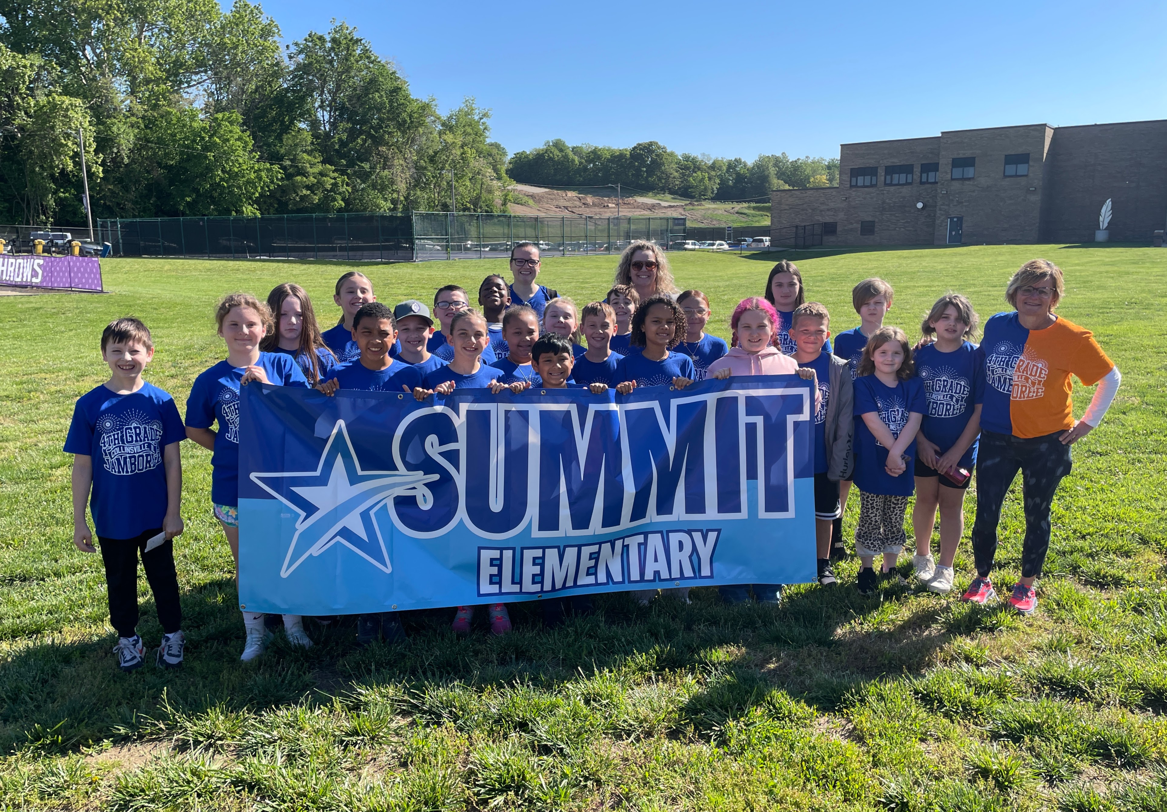 A group of students and adults pose for a photo outdoors, holding a banner that reads "SUMMIT ELEMENTARY".