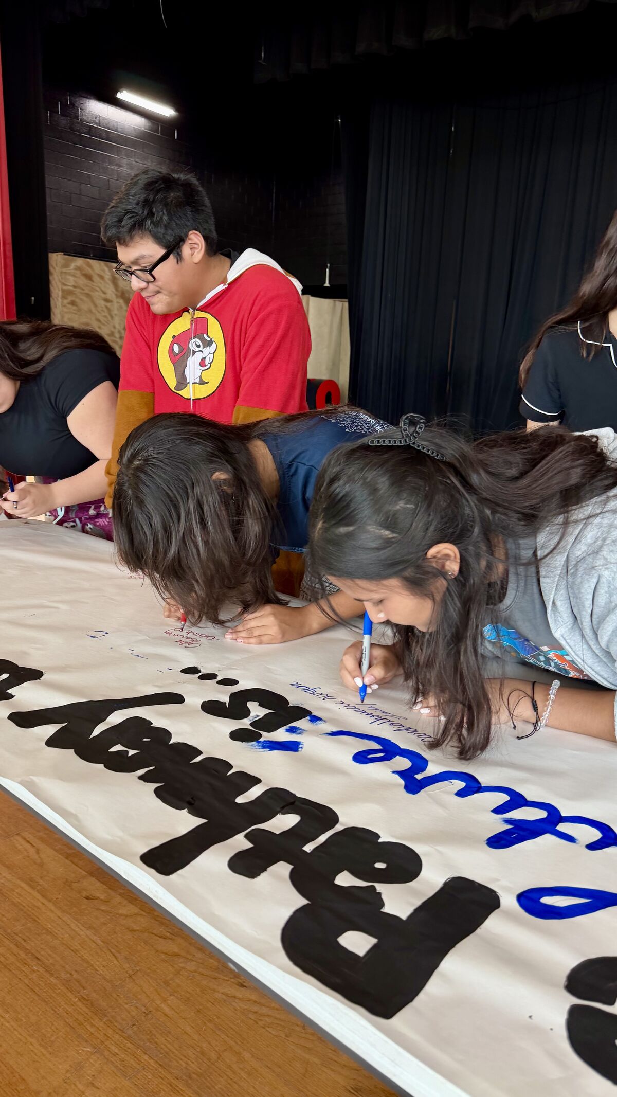 A group of students gather around a long table, working together to write on a large banner.