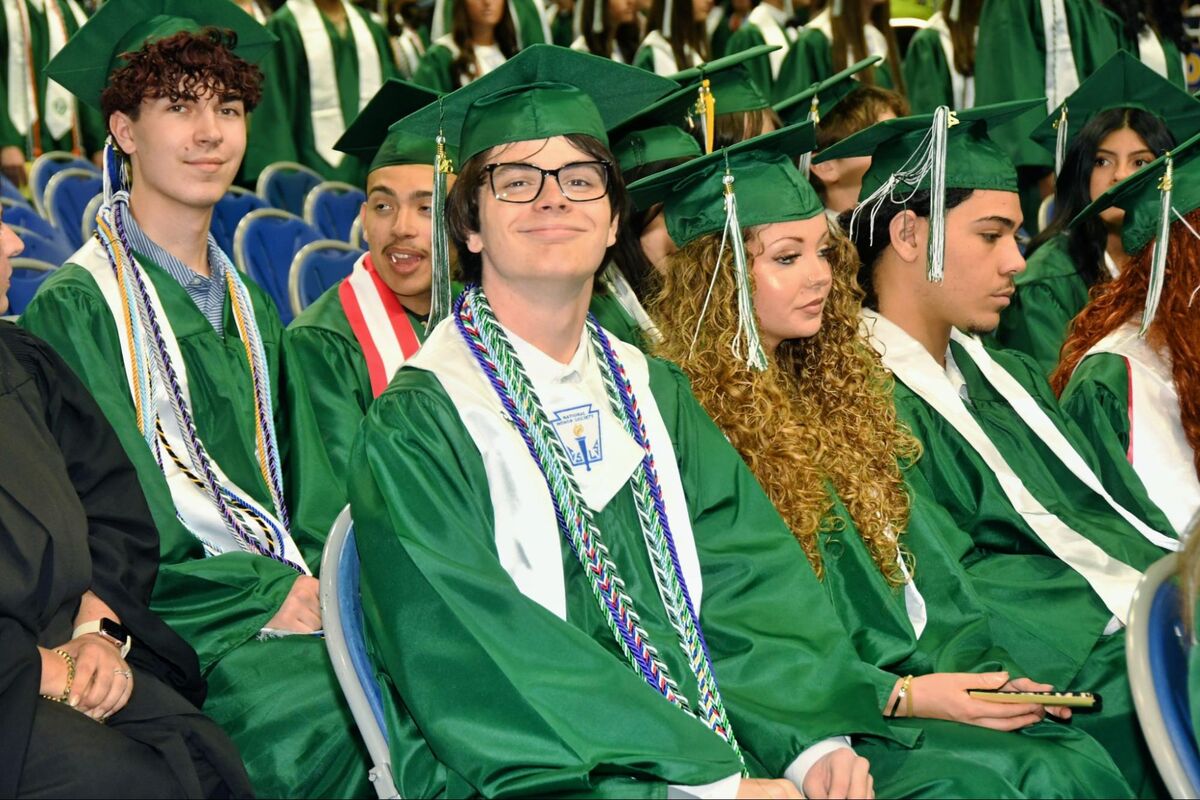 Graduates in green gowns and caps sit in rows, anticipating a ceremony.