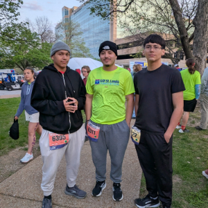 Three young men stand together outdoors, wearing race bibs.