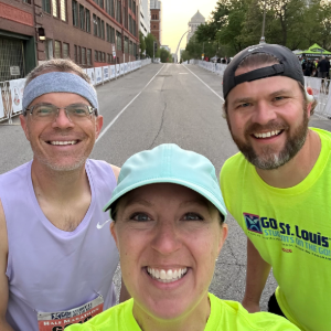 Three smiling people in athletic wear take a selfie on a street, with a city skyline in the background.