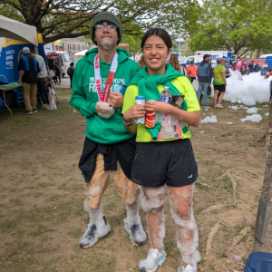 Two smiling participants, covered in foam, pose after an outdoor event.