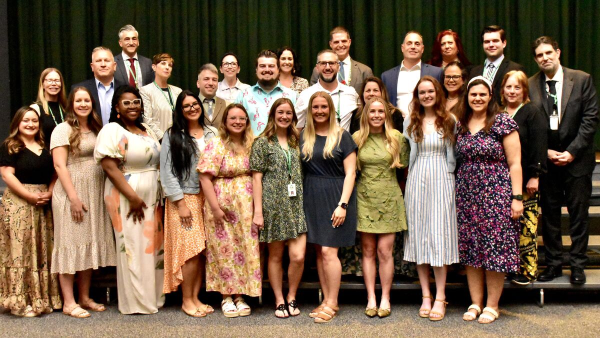 A diverse group of people, men and women, pose for a photo in front of a green backdrop.