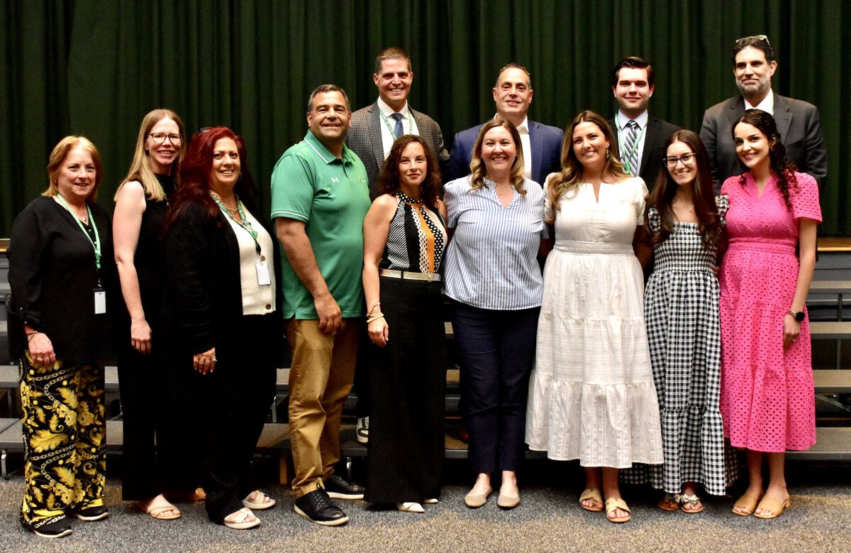 A diverse group of adults stands together, smiling for a photo in front of a dark green curtain.