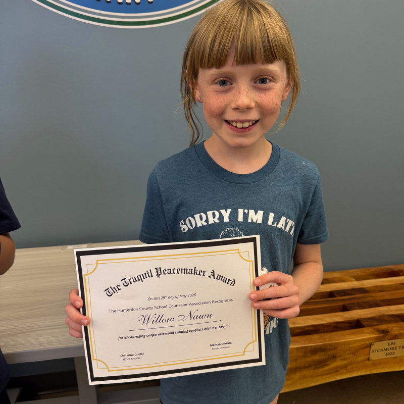 A young girl smiles proudly while holding a certificate for "The Tranquil Peacemaker Award".