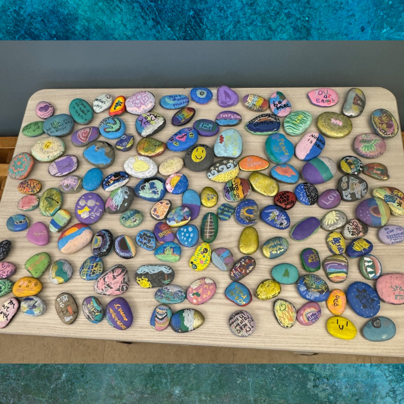 A collection of colorful, painted rocks with positive messages and designs are displayed on a wooden surface.