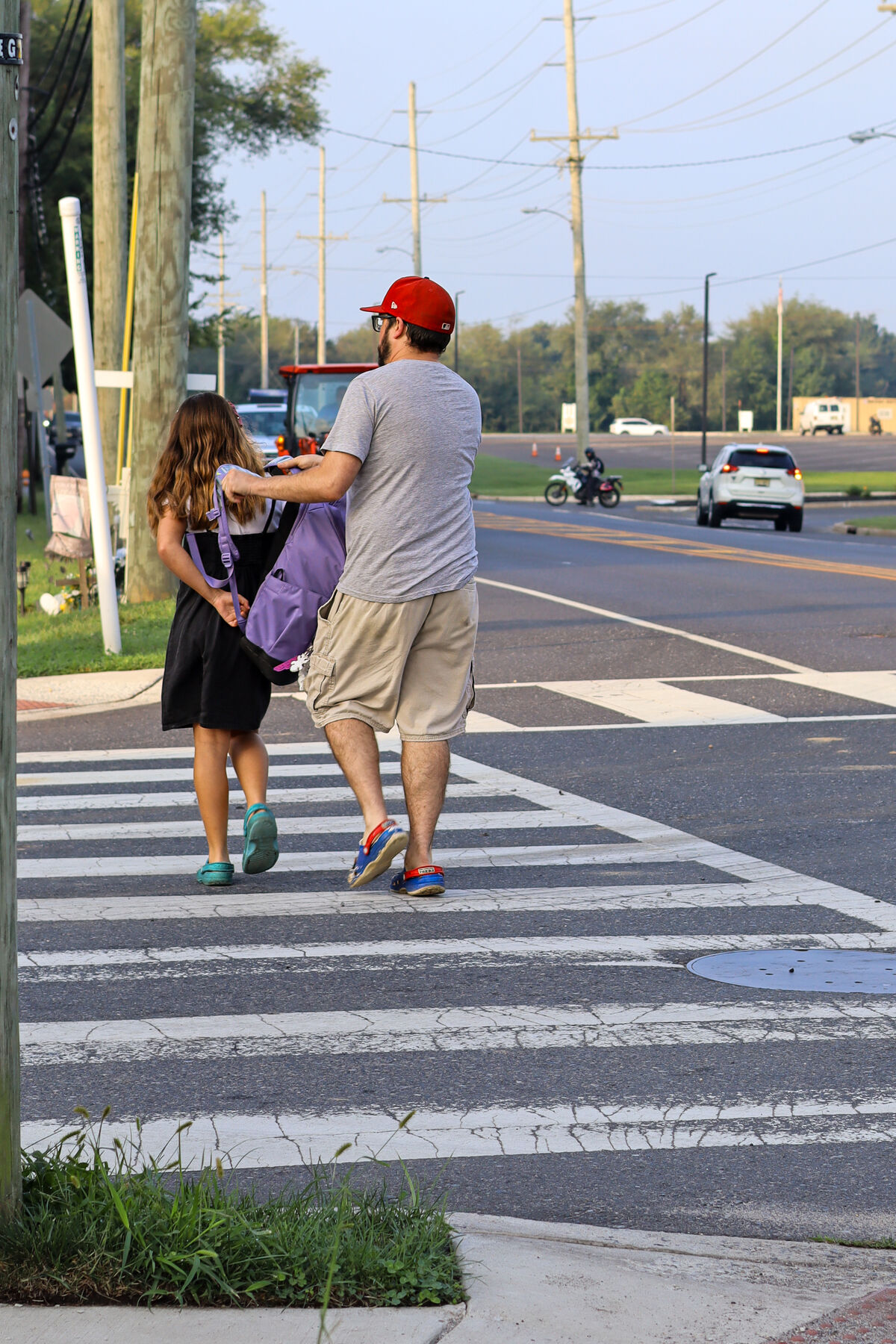 A man and a young girl walk across a marked crossroad on a paved street.