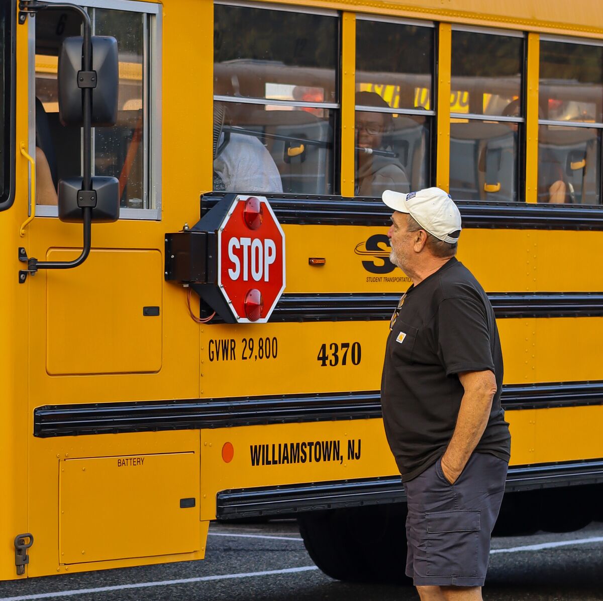 A person wearing a white cap stands beside a bright yellow school bus.