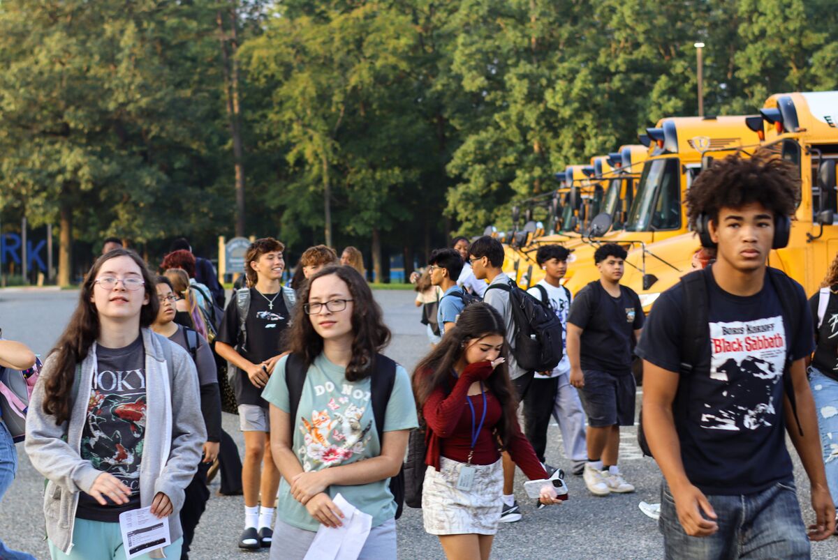 A group of students walking in a parking lot near a line of parked yellow school buses.