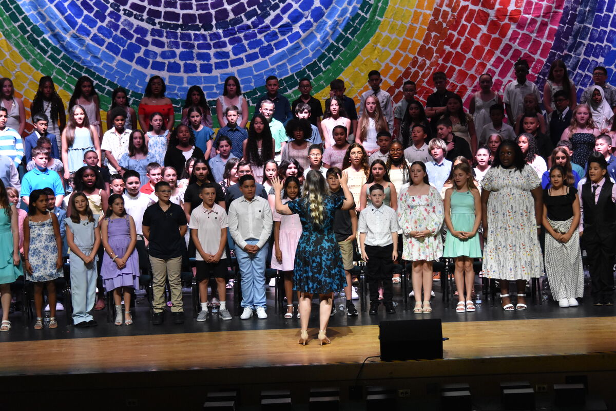 A diverse group of children stand on a stage in front of a colorful, abstract backdrop.