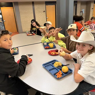 A group of students smiling at the camera while sitting around a cafeteria table during lunch.