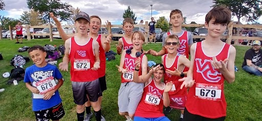 A group of young runners in matching red and white singlets pose together outdoors on a grassy hill.